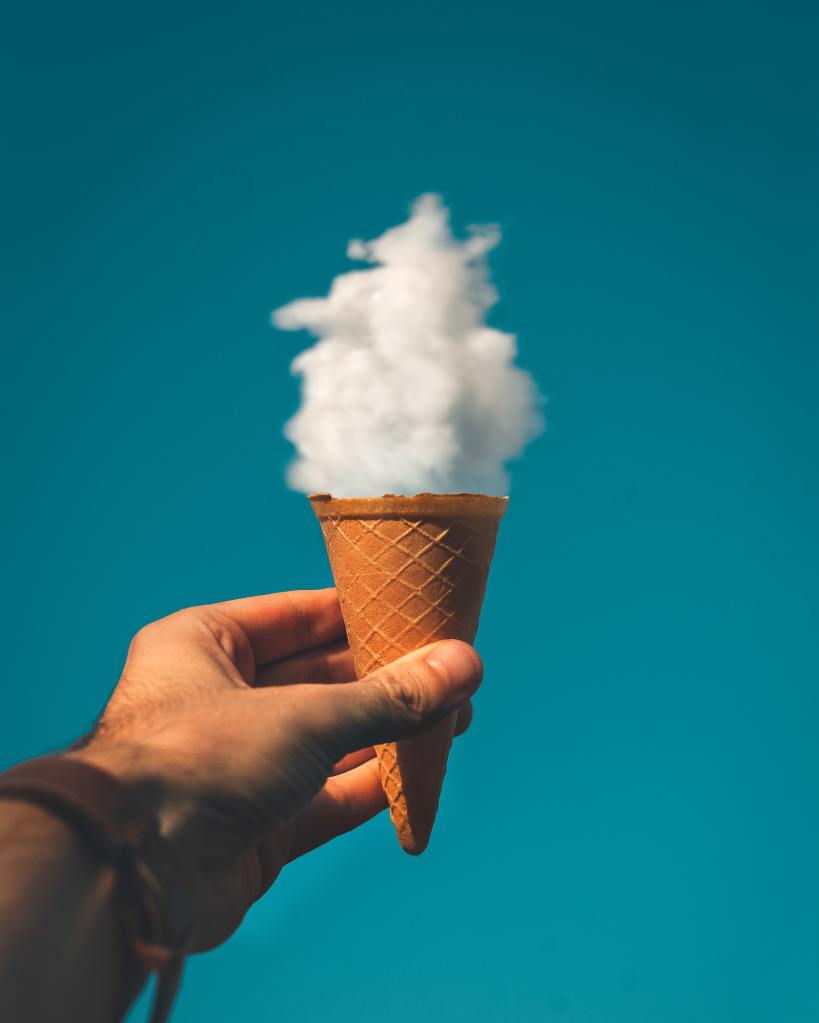 Hand Holding Ice Cream Cone Under Cloud 